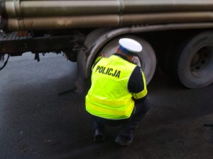 policjant w kamizelce odblaskowej kuca przy osi pojazdu