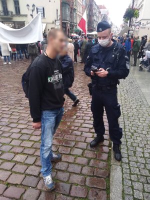 ulica, umundurowany policjant legitymuje mężczyznę bez maseczki