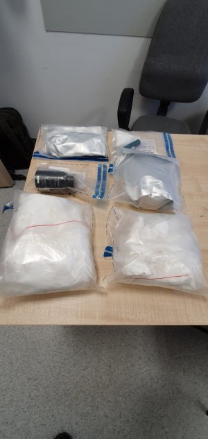 Zdjęcie  zabezpieczonych przez policjantów kryminalnych  trzech kilogramów narkotyków , policjant przekładający narkotyki n a biurku i  liczący środki anaboliczne.