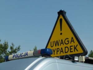 Zdjęcie poglądowe - znak  trójkąta i na żółtym tle czarny napis  UWAGA WYPADEK  i wykrzyknik, umieszczony na radiowozie. Na pierwszym planie galeryjka z napisem POLICJA.
