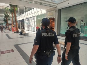 dwójka umundurowanych policjantów idzie alejką w galerii handlowej