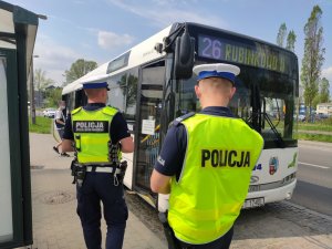 dwóch umundurowanych policjantów podchodzi do autobusu mzk na przystanku