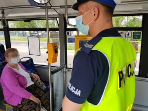 umundurowany policjant wewnątrz autobusu mzk, na siedzeniach siedzą ludzie